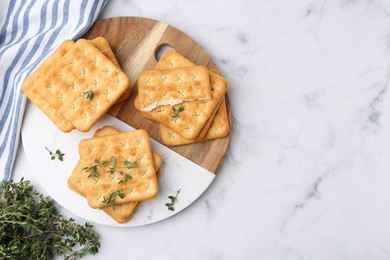 Photo of Tasty salty crackers with thyme on white marble table, top view. Space for text