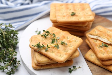 Photo of Tasty salty crackers with thyme on white table, closeup