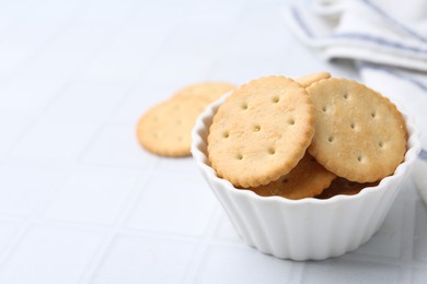 Photo of Tasty salty crackers on white tiled table, closeup. Space for text