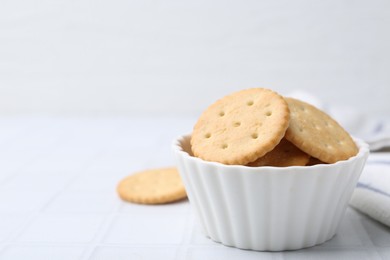 Photo of Tasty salty crackers on white tiled table, closeup. Space for text