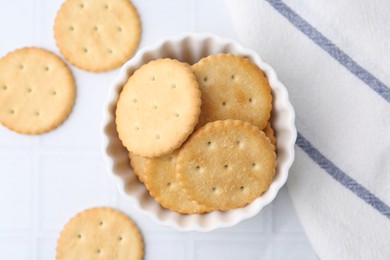 Photo of Tasty salty crackers on white tiled table, flat lay