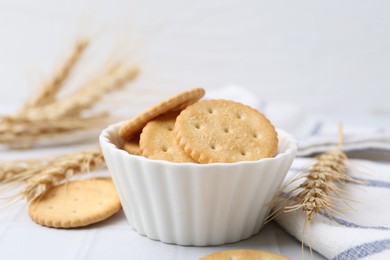 Photo of Tasty salty crackers with wheat spikes on white tiled table, closeup
