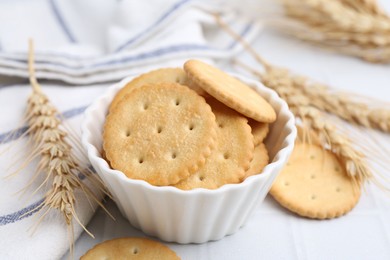 Photo of Tasty salty crackers with wheat spikes on white tiled table, closeup