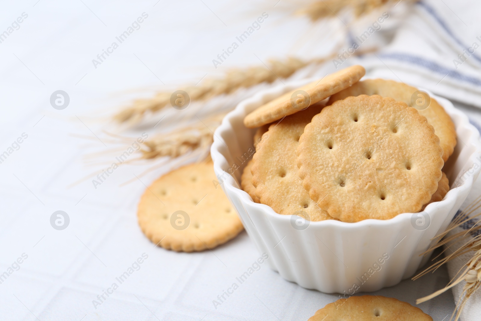 Tasty salty crackers with wheat spikes on white tiled table, closeup. Space for text Photo of Tasty salty crackers with wheat spikes on white tiled table, closeup. Space for text