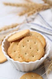 Photo of Tasty salty crackers with wheat spikes on white table, closeup