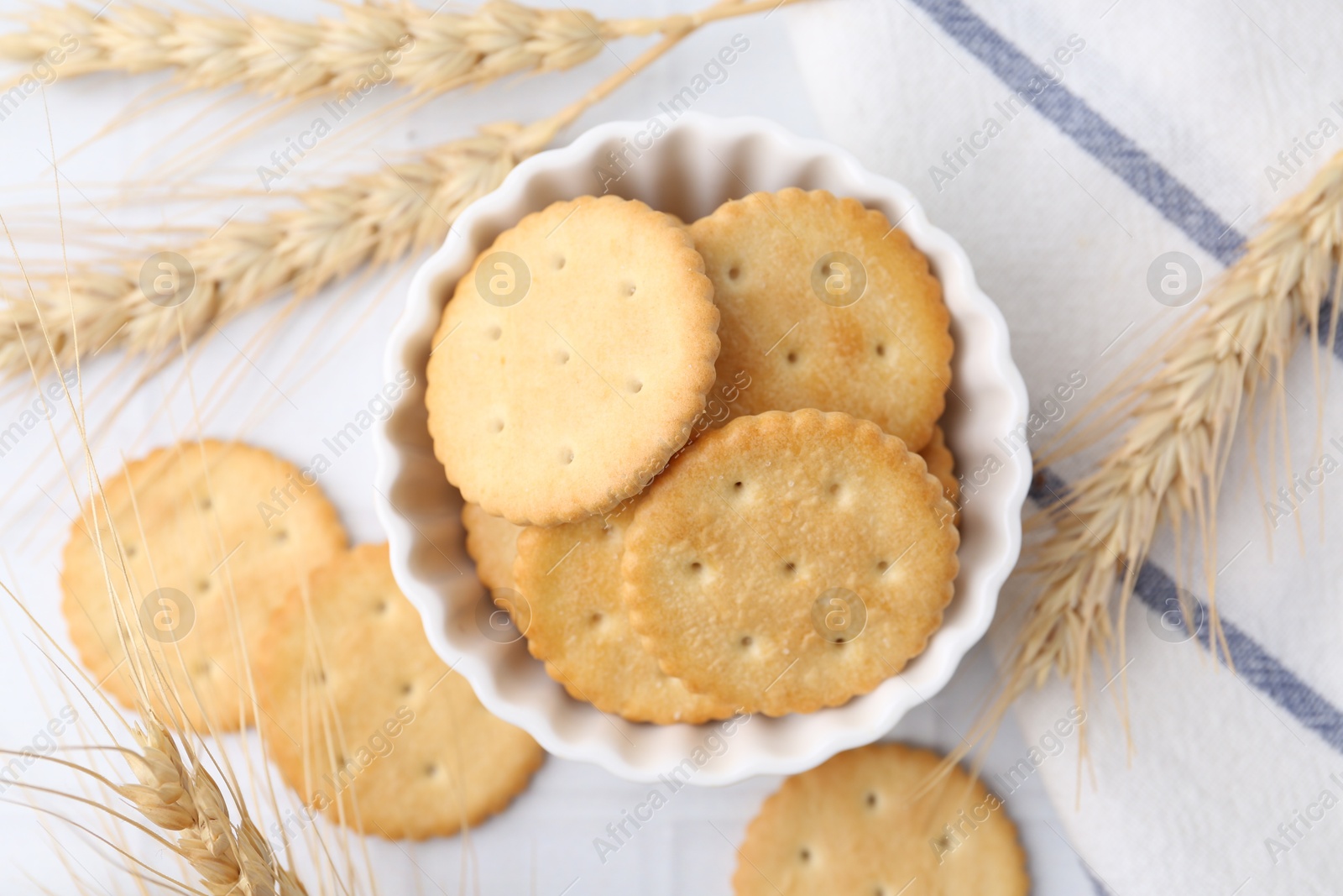 Tasty salty crackers with wheat spikes on white tiled table, flat lay Photo of Tasty salty crackers with wheat spikes on white tiled table, flat lay