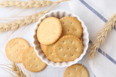 Photo of Tasty salty crackers with wheat spikes on white tiled table, flat lay