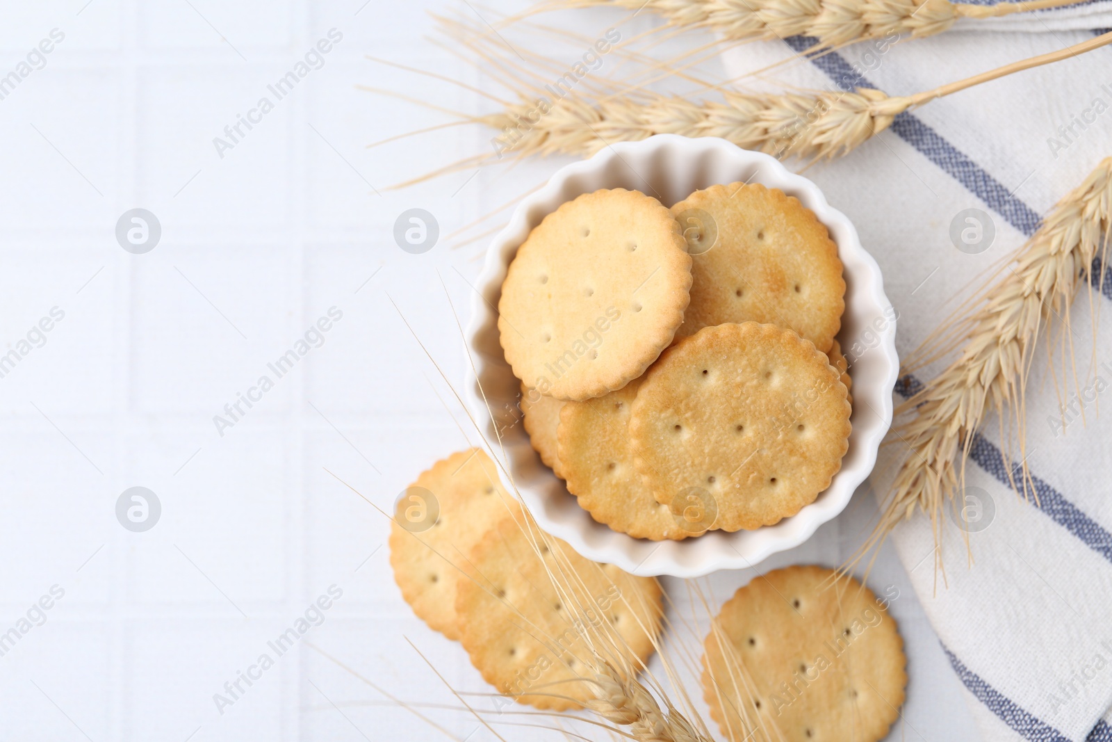 Tasty salty crackers with wheat spikes on white tiled table, flat lay. Space for text Photo of Tasty salty crackers with wheat spikes on white tiled table, flat lay. Space for text