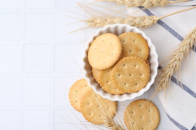 Photo of Tasty salty crackers with wheat spikes on white tiled table, flat lay. Space for text