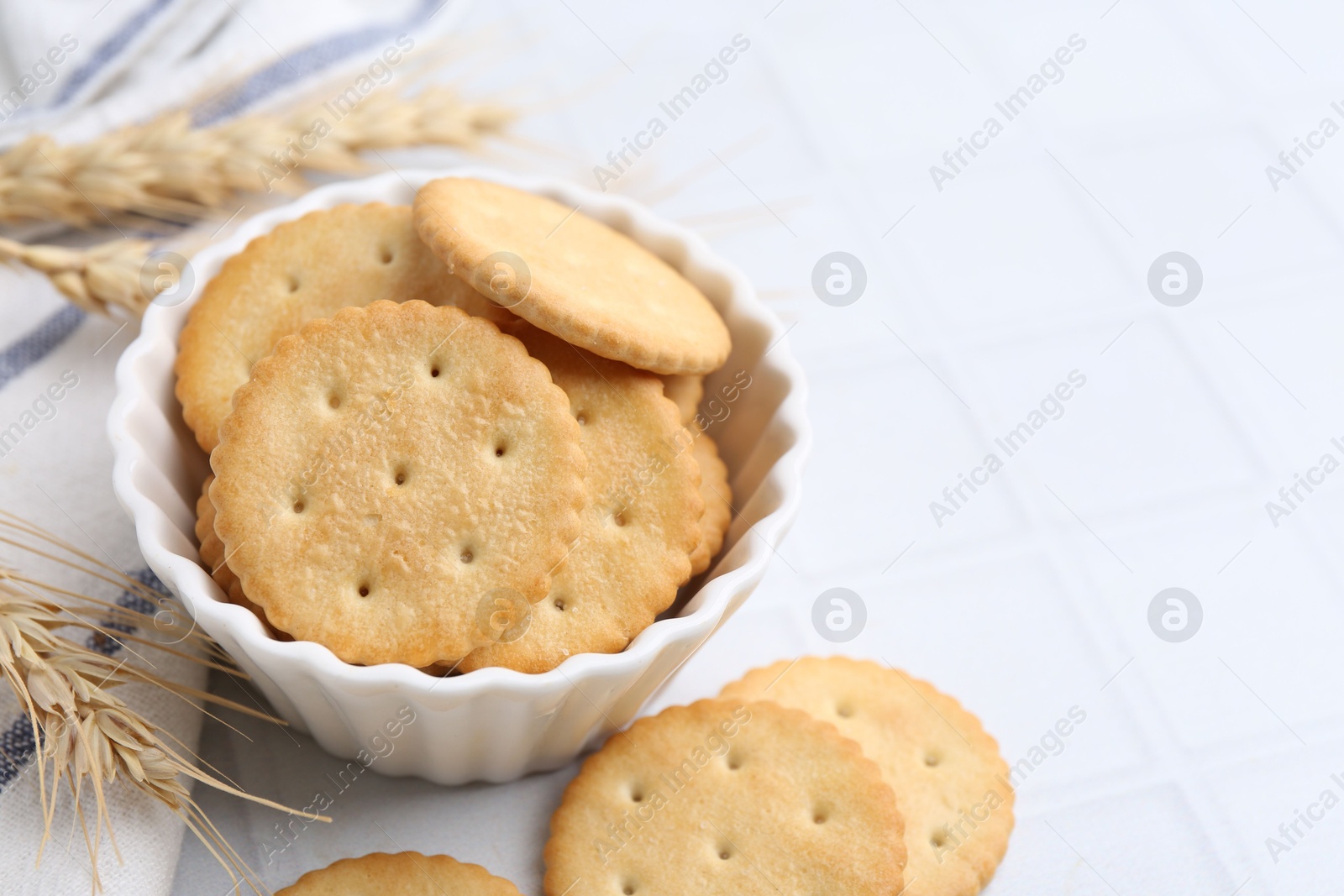 Tasty salty crackers with wheat spikes on white tiled table, closeup. Space for text Photo of Tasty salty crackers with wheat spikes on white tiled table, closeup. Space for text