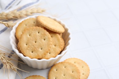 Photo of Tasty salty crackers with wheat spikes on white tiled table, closeup. Space for text