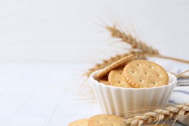 Photo of Tasty salty crackers with wheat spikes on white tiled table. Space for text