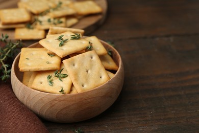 Photo of Tasty salty crackers with thyme on wooden table, closeup. Space for text