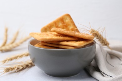 Photo of Tasty salty crackers with wheat spikes on white table, closeup