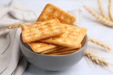 Photo of Tasty salty crackers with wheat spikes on white table, closeup