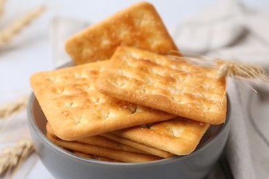 Photo of Tasty salty crackers with wheat spikes on white table, closeup