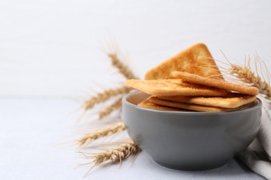 Photo of Tasty salty crackers with wheat spikes on white table. Space for text