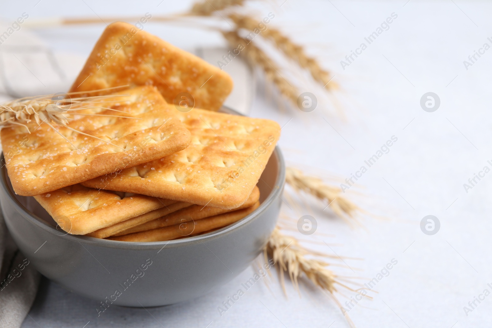 Tasty salty crackers with wheat spikes on white table, closeup. Space for text Photo of Tasty salty crackers with wheat spikes on white table, closeup. Space for text