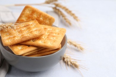 Photo of Tasty salty crackers with wheat spikes on white table, closeup. Space for text