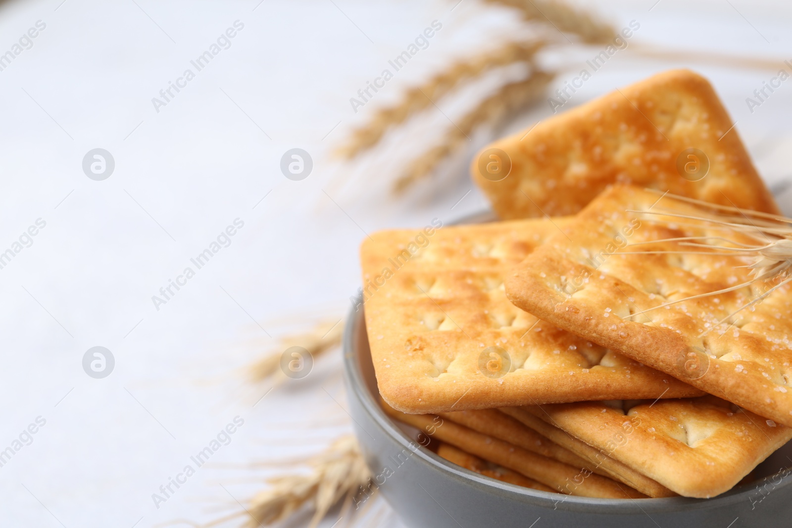 Tasty salty crackers with wheat spikes on white table, closeup. Space for text Photo of Tasty salty crackers with wheat spikes on white table, closeup. Space for text