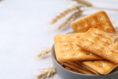 Photo of Tasty salty crackers with wheat spikes on white table, closeup. Space for text