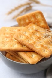 Photo of Tasty salty crackers with wheat spikes on white table, closeup