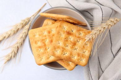 Photo of Tasty salty crackers with wheat spikes on white table, top view