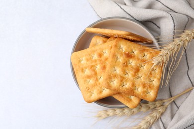 Photo of Tasty salty crackers with wheat spikes on white table, top view. Space for text
