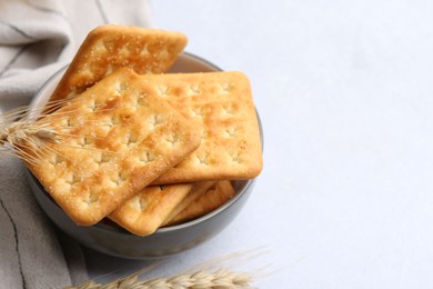Photo of Tasty salty crackers with wheat spikes on white table, closeup. Space for text