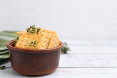 Photo of Tasty salty crackers with thyme on white wooden table, closeup. Space for text