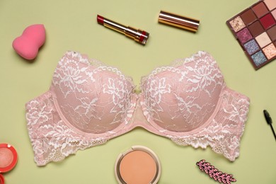 Photo of Beautiful lace bra, makeup products, sponge and hair clip on light green background, flat lay