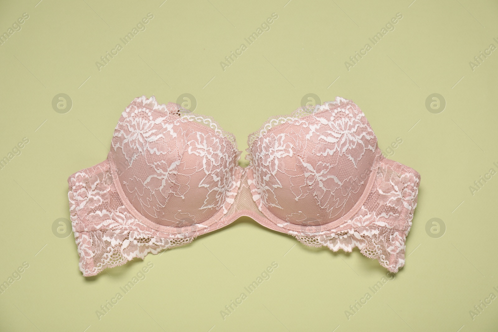 Photo of Beautiful beige lace bra on light green background, top view
