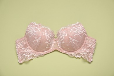 Photo of Beautiful beige lace bra on light green background, top view
