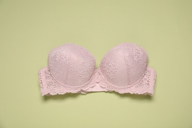 Photo of Beautiful beige lace bra on light green background, top view