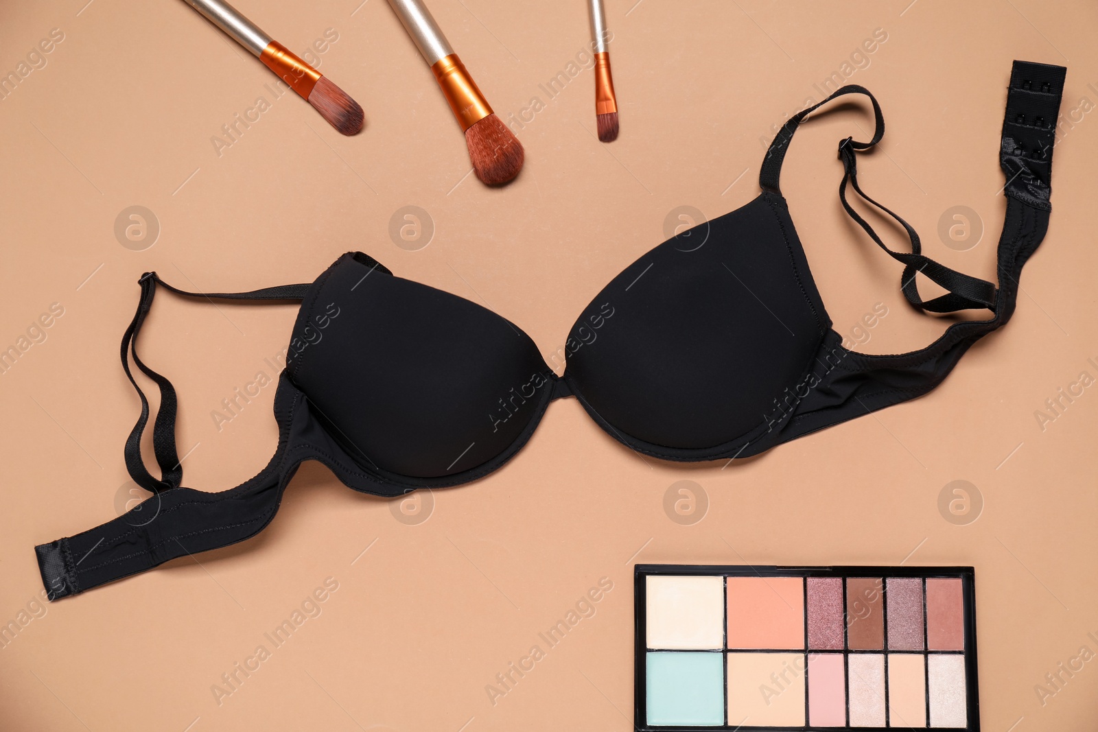 Beautiful black bra, eyeshadow brushes and color palette on beige background, flat lay Photo of Beautiful black bra, eyeshadow brushes and color palette on beige background, flat lay
