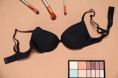 Photo of Beautiful black bra, eyeshadow brushes and color palette on beige background, flat lay