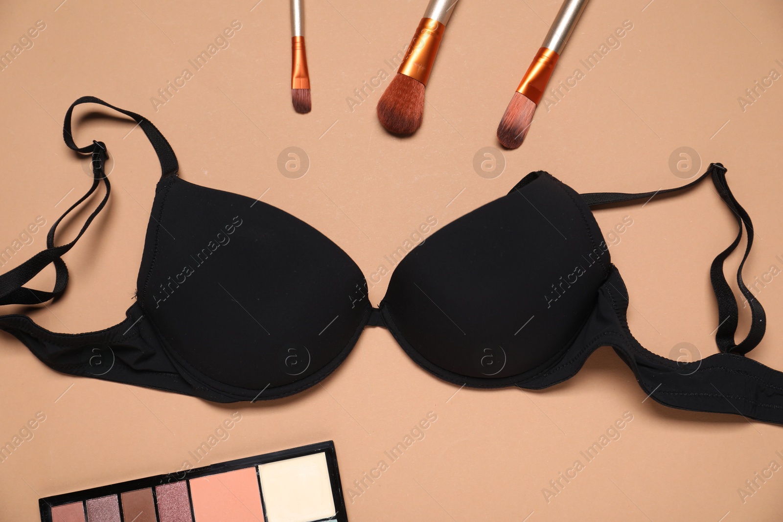 Photo of Beautiful black bra, eyeshadow brushes and color palette on beige background, flat lay