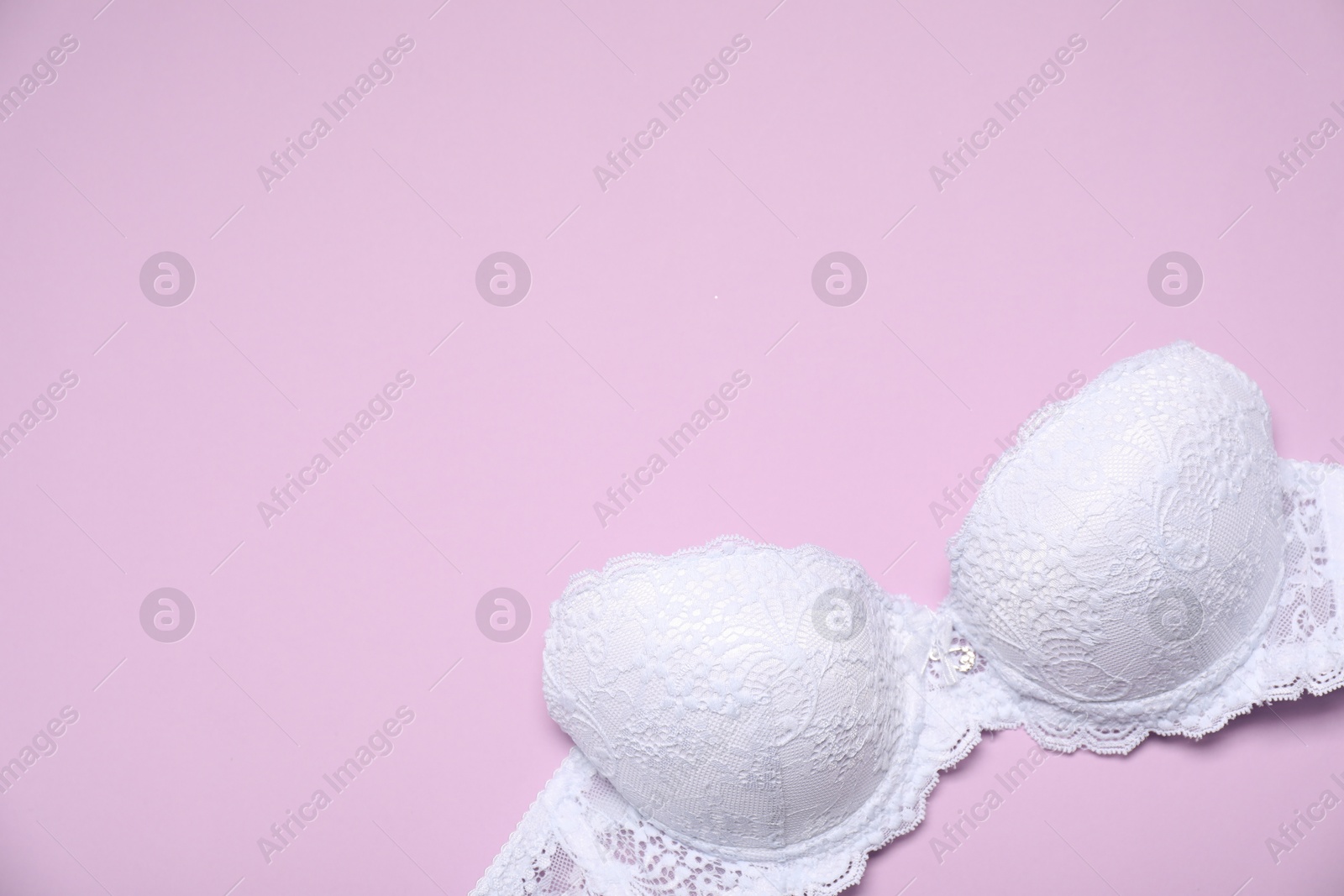 Photo of Beautiful white lace bra on pink background, top view. Space for text