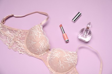Photo of Beautiful beige lace bra, perfume bottle and lipstick on pink background, flat lay