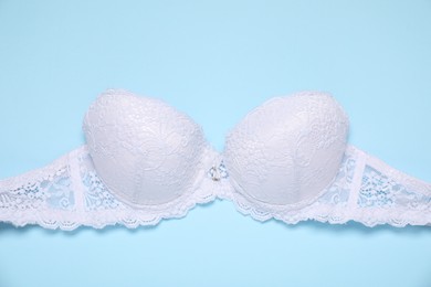 Photo of Beautiful white lace bra on light blue background, top view