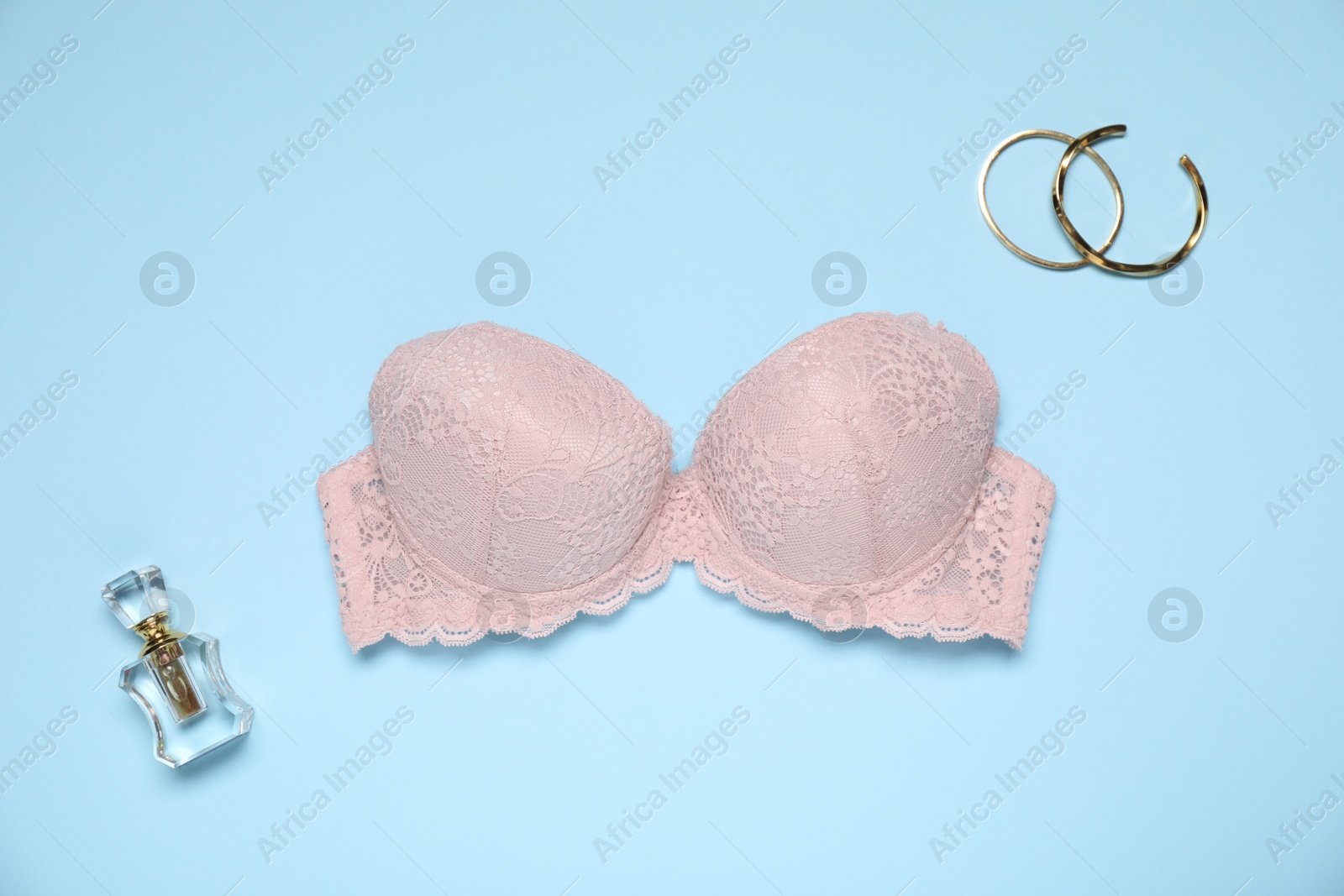 Beautiful beige lace bra, perfume bottle and bracelets on light blue background, flat lay Photo of Beautiful beige lace bra, perfume bottle and bracelets on light blue background, flat lay