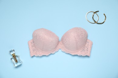 Photo of Beautiful beige lace bra, perfume bottle and bracelets on light blue background, flat lay