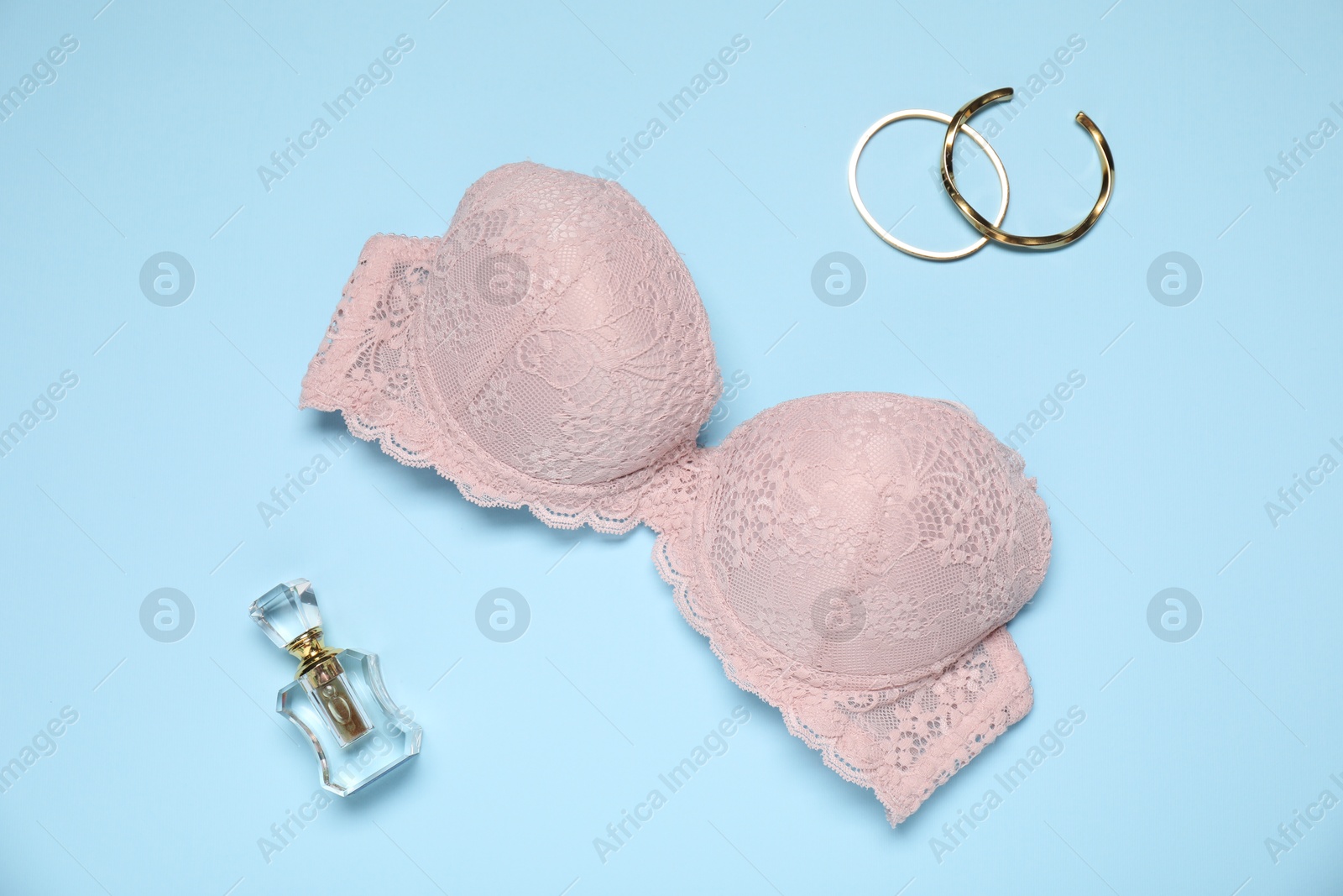 Beautiful beige lace bra, perfume bottle and bracelets on light blue background, flat lay Photo of Beautiful beige lace bra, perfume bottle and bracelets on light blue background, flat lay