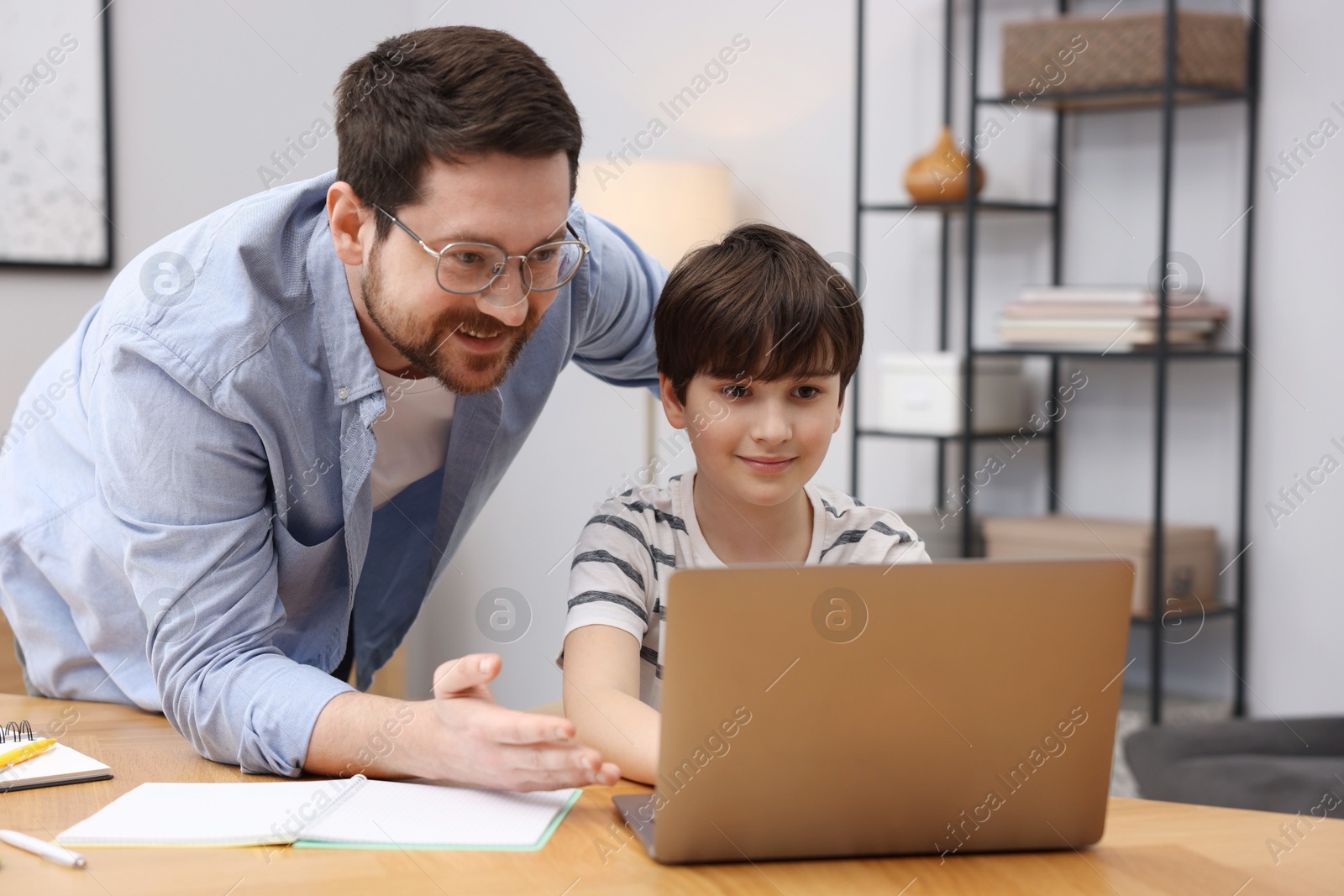 Father helping his son with homework at wooden table indoors Photo of Father helping his son with homework at wooden table indoors