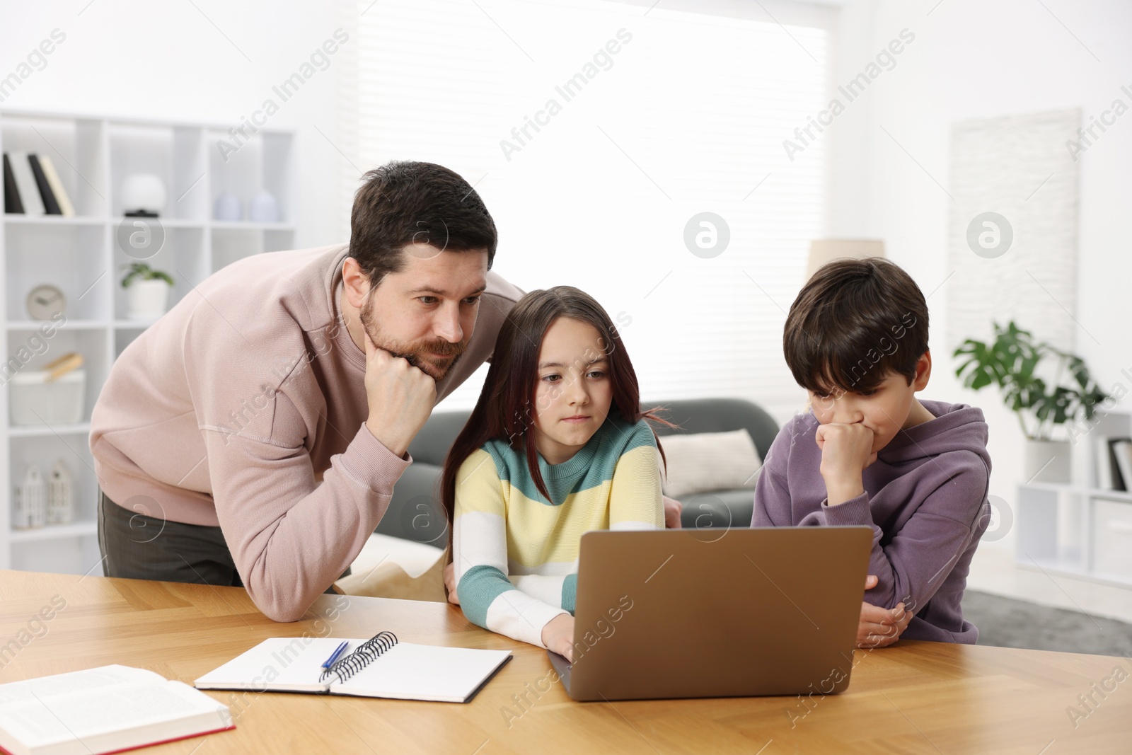 Father helping his kids with homework at wooden table indoors Photo of Father helping his kids with homework at wooden table indoors