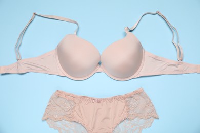 Photo of Beautiful beige bra and panties on light blue background, flat lay