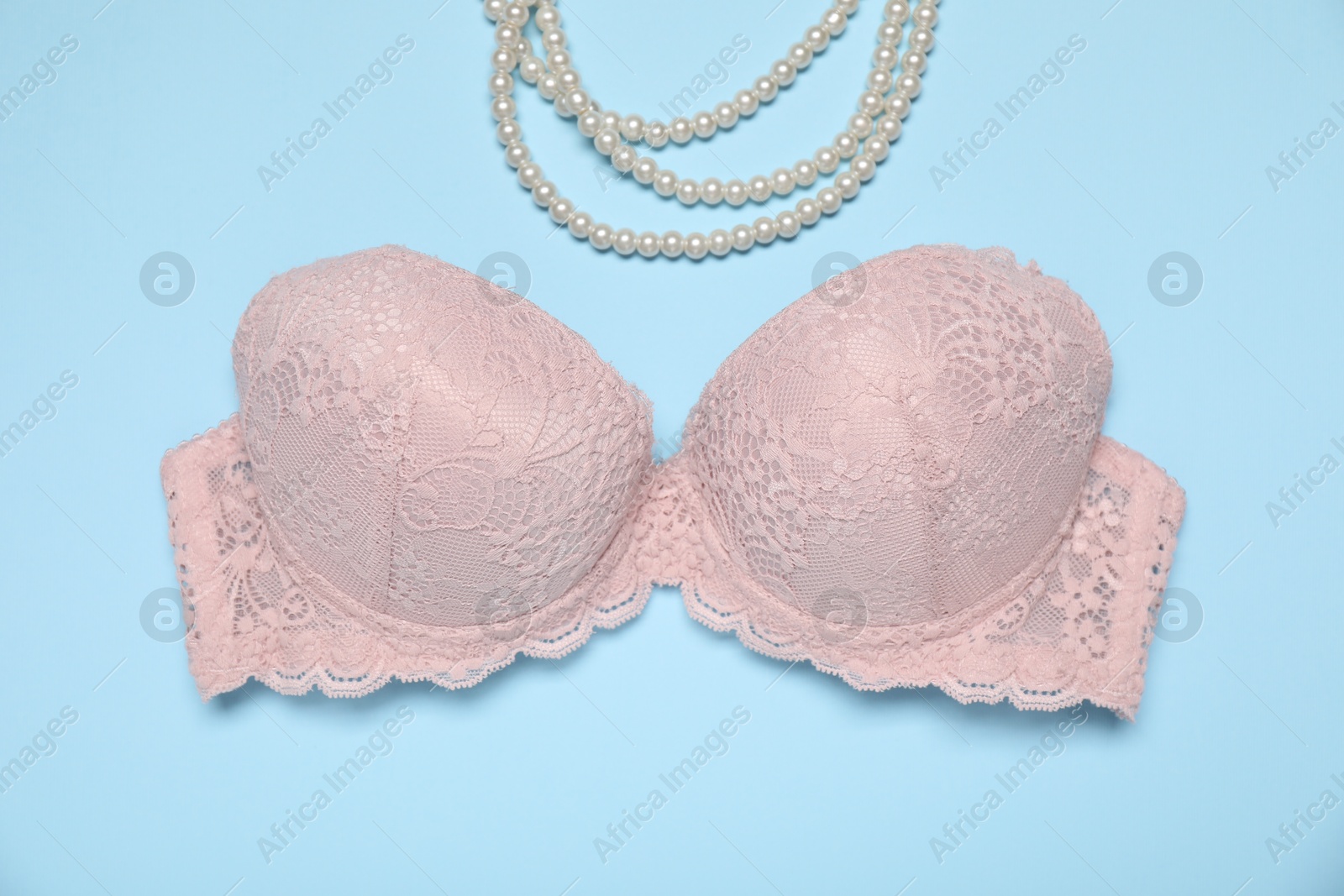 Beautiful beige lace bra and pearl necklace on light blue background, flat lay Photo of Beautiful beige lace bra and pearl necklace on light blue background, flat lay