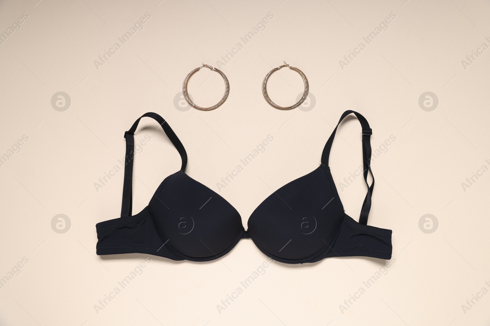 Photo of Black bra and earrings on beige background, flat lay