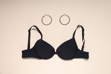 Photo of Black bra and earrings on beige background, flat lay