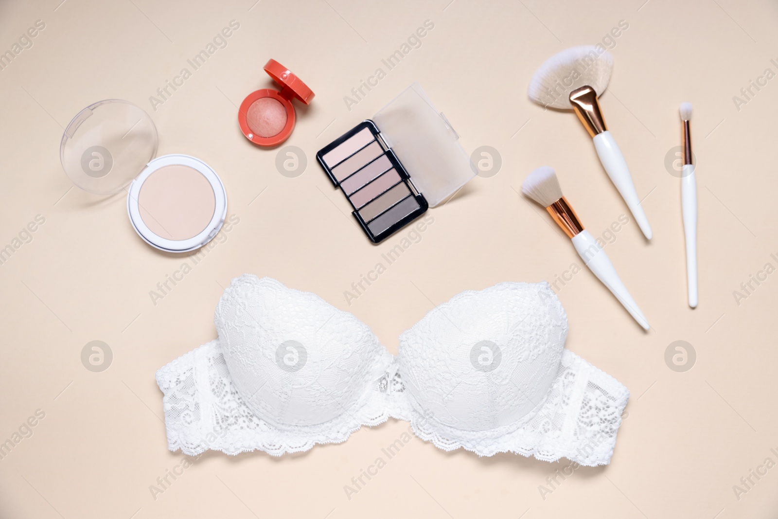 Flat lay composition with white lace bra and cosmetic products on beige background Photo of Flat lay composition with white lace bra and cosmetic products on beige background
